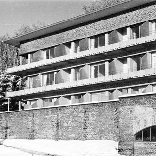 Here's a brief summary of the image: Multistory brick building with balconies, snow-covered landscape.