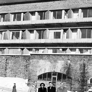 Group stands in snow before a large brick building.