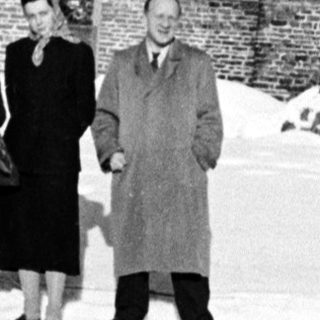 Group stands in snow before a large brick building.