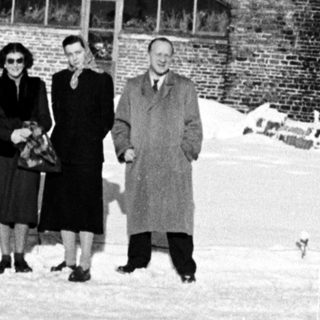 Group stands in snow before a large brick building.