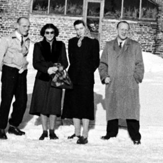 Group stands in snow before a large brick building.
