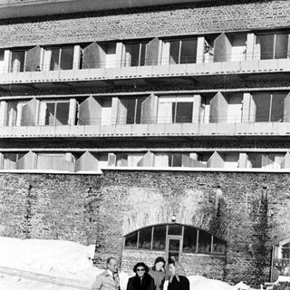 Four people stand in snow before a large brick building.