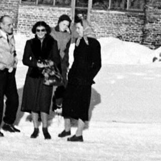 Four people stand in snow before a large brick building.