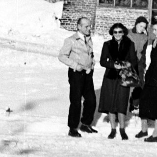 Four people stand in snow before a large brick building.