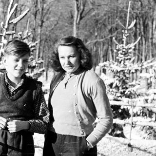 Two children stand in a snowy, wooded landscape.