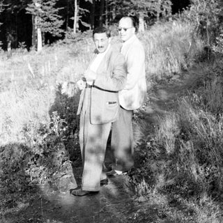 Two men in suits stand on a grassy path.