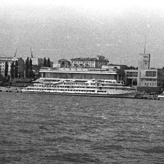 Black and white image of boats and buildings along a river.