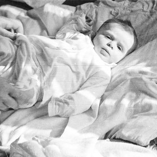 Here's a brief summary of the image: Baby in a basket, wrapped in white fabric.