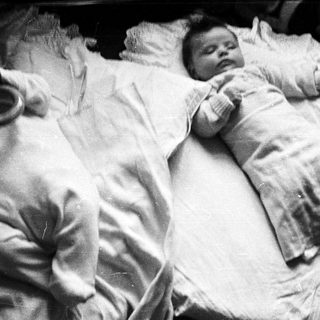 Two infants sleep peacefully in matching white clothing.
