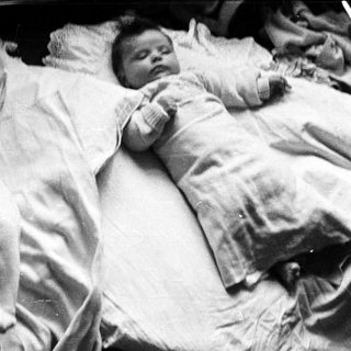 Two infants sleep peacefully in matching white clothing.