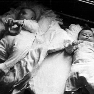 Here's a brief summary of the image: Baby lying in a crib, covered in white fabric.