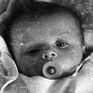 Here's a brief summary of the image: Baby with pacifier, nestled in a lace-trimmed blanket.