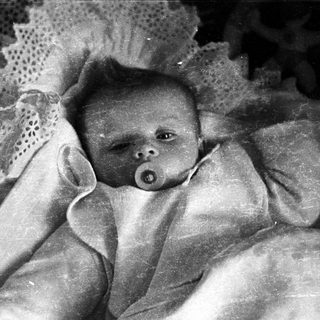 Here's a brief summary of the image: Baby with pacifier, nestled in a lace-trimmed blanket.