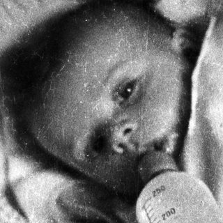 Infant lying down, receiving nourishment from a feeding tube.