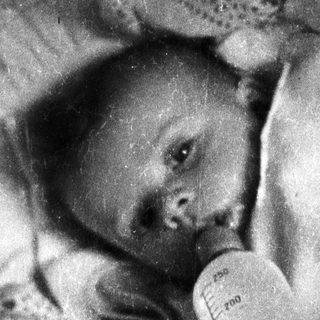 Infant lying down, receiving nourishment from a feeding tube.