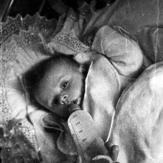 Infant lying down, receiving nourishment from a feeding tube.