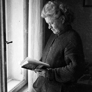 Man lies reading a book near a window.