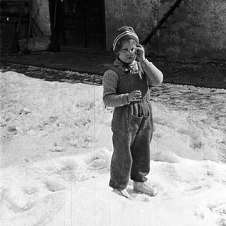 Child in winter clothing stands in snowy yard.