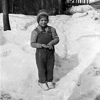 Child stands in snowy yard near a wooden fence.