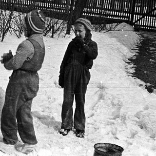 Two children stand near a snowman in a snowy yard.