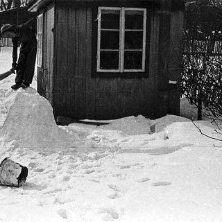 Boy climbs snow pile near a building in winter.