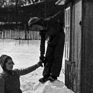 Boy climbs snow pile near a building in winter.