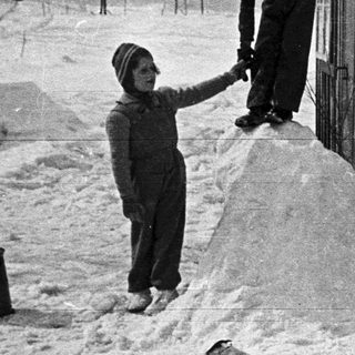 Boy climbs snow pile near a building in winter.