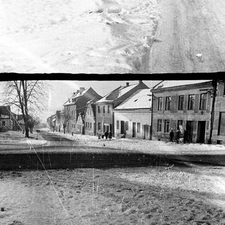 Winter street scene with buildings and snowy hillside.