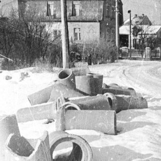 Snow-covered road with tracks and houses in the background.
