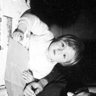 Here's a brief summary of the image: Man baking, child playing with a box and fan.