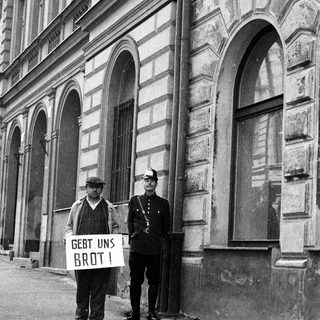 Beggar with sign confronts police officer on street.