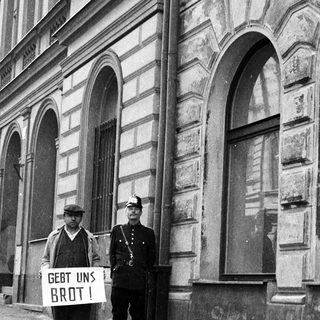 Beggar with sign confronts police officer on street.
