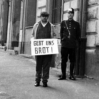 Beggar with sign confronts police officer on street.