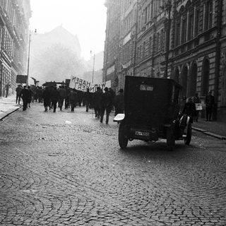 A procession or demonstration takes place on a cobblestone street.