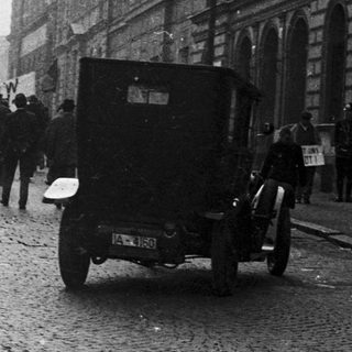 A procession or demonstration takes place on a cobblestone street.
