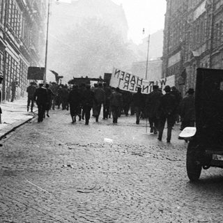 A procession or demonstration takes place on a cobblestone street.