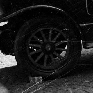 Man assists driver of vintage car on cobblestone street.