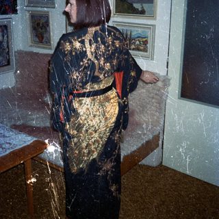 Woman in robe stands in room with artwork.
