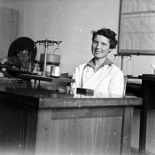 Woman in lab coat stands behind a laboratory table.