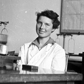 Woman in lab coat stands behind a laboratory table.