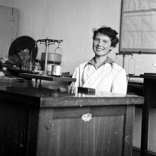 Woman in lab coat smiles behind a laboratory workbench.