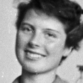 Woman in lab coat smiles behind a laboratory workbench.