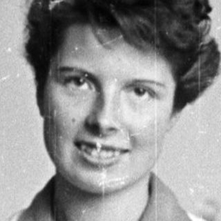 Woman in lab coat smiles behind a workbench.