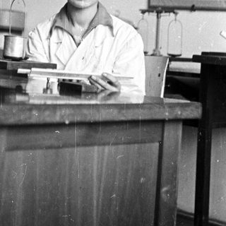 Woman in lab coat smiles behind a workbench.