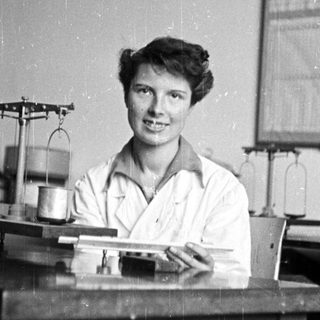 Woman in lab coat smiles behind a workbench.