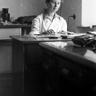 Woman in lab coat seated at a table.