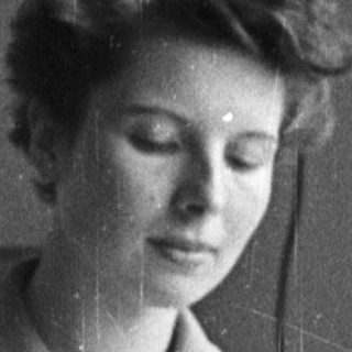 Woman in lab coat seated at a table.