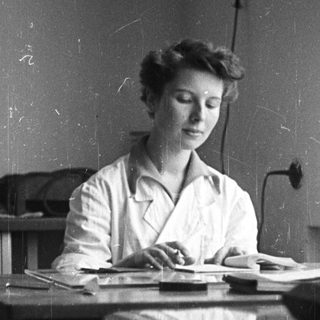 Woman in lab coat seated at a table.
