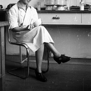 Woman in lab coat seated, holding a flask.