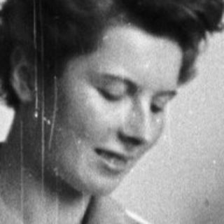 Woman in lab coat seated, holding a flask.